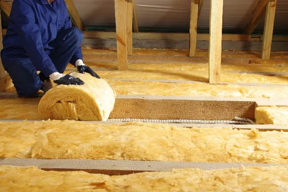 Person verlegt Dämmwolle auf Dachboden